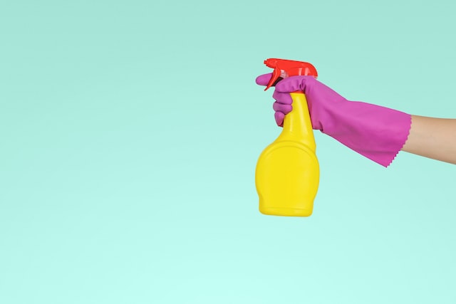 A person wearing hand gloves holding cleaning bottle